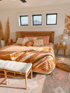 a bedroom with a bed, pillows and rugs on the floor in front of two windows