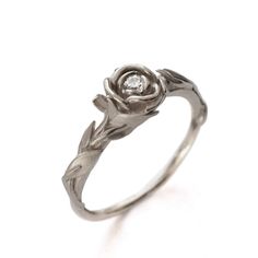 a white gold ring with a diamond in the center and leaves on each side,