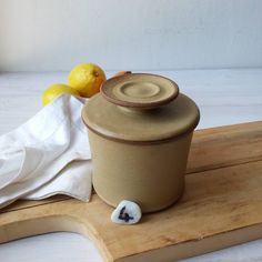 a ceramic container sitting on top of a cutting board next to lemons and a towel