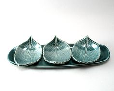 three leaf shaped dishes sitting on top of a green plate