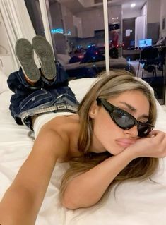 a woman laying on top of a bed wearing sunglasses