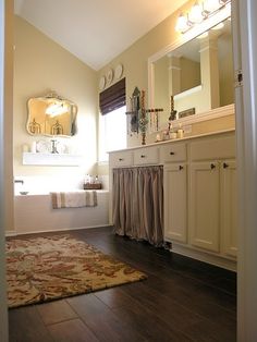 a bathroom with white cabinets and wooden floors is seen through the doorway to another room