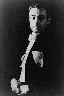 a black and white photo of a man in a tuxedo with his hand on his chin