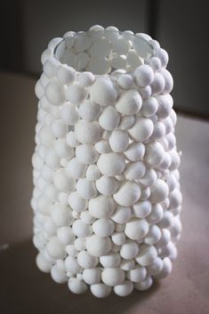 a white vase sitting on top of a table covered in lots of small round balls