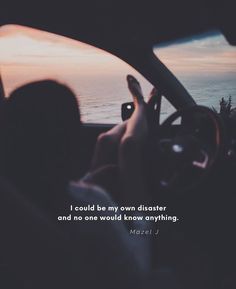 a person sitting in a car with their hand on the steering wheel and an ocean view behind them