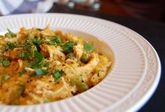 a white plate topped with macaroni and cheese covered in parsley on top of a table