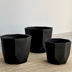 three black planters sitting on top of a rug next to each other in front of a white wall