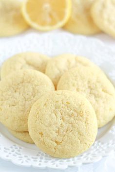 three lemon cookies on a white plate next to sliced lemons and a glass of orange juice