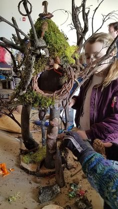 two women are working on a sculpture in the shape of a tree with moss growing out of it