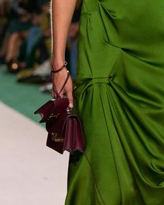 a woman in a green dress is holding a purse and walking down the catwalk