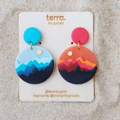 two colorful earrings with mountains on them sitting on a card that says terra, by serh