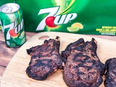 three steaks on a wooden cutting board next to a can of 7up soda