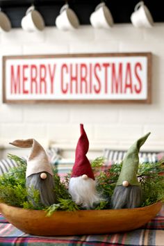 three gnome figurines sitting on top of a wooden bowl filled with greenery