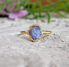 a gold ring with a blue druzby stone in the center on a rock