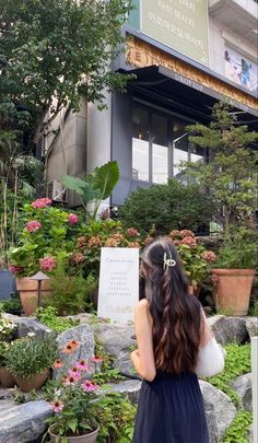 a woman standing in front of a building with lots of plants