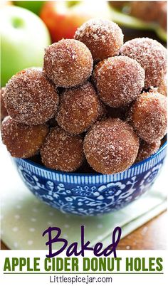 a blue bowl filled with sugar covered donuts on top of a table next to apples