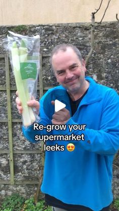 a man holding up a bunch of celery stalks in front of a brick wall