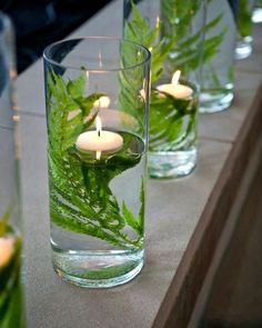 candles are lit in glass vases filled with water and leaves on a table top