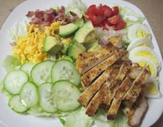 a white plate topped with meat, cucumbers and tomatoes next to sliced eggs