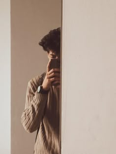 a man standing in front of a white wall holding a cell phone to his face