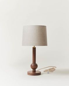 a wooden table lamp with a white shade on it and a cord plugged into the base