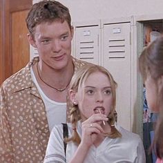 a man and woman standing next to each other in front of lockers eating food