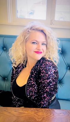 a woman with blonde hair sitting at a table in front of a blue velvet chair