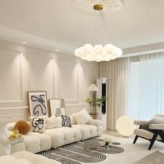 a living room filled with white furniture next to a large window and a chandelier