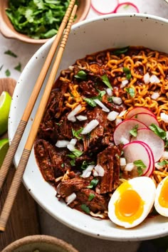 a bowl filled with noodles, meat and vegetables next to chopsticks on a table