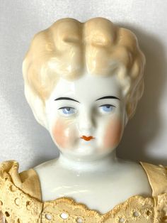 a white porcelain busturine with blonde hair and blue eyes wearing a yellow dress