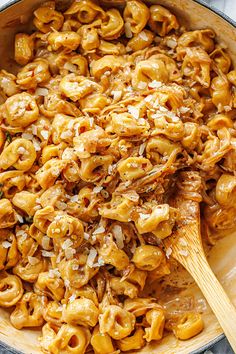 a skillet filled with macaroni and cheese being stirred by a wooden spoon