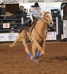 a woman riding on the back of a brown horse in an arena at a rodeo