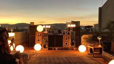 two people sitting in front of speakers on top of a roof at night with the sun setting behind them