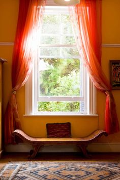 a window with red curtains and a bench in front of it on a carpeted floor