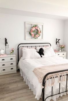 a bedroom with white bedding and pink flowers on the headboard, dressers and chest of drawers