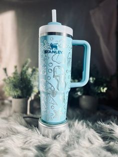 a blue and white travel mug sitting on top of a fur covered floor next to potted plants