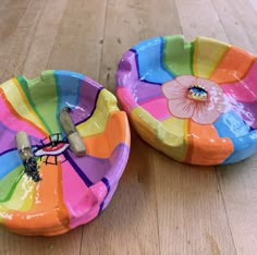 two brightly colored bowls sitting on top of a wooden table next to each other, one with a flower painted on it