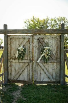 an old wooden gate with two wreaths and flowers on the doors is shown in front of a grassy field