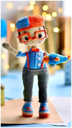 a crocheted doll is posed on a piece of paper with glasses and an orange bow tie