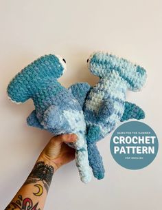 two crocheted stuffed animals in the shape of sharks are held up by someone's hand