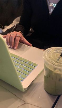 a woman sitting at a table using a laptop computer with a drink in front of her