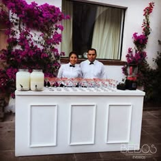 two people standing behind a table with glasses on it