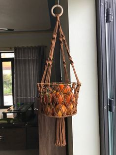 a hanging basket filled with oranges on top of a wooden table next to a window