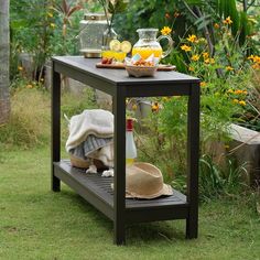 an outdoor table with drinks and food on it in the grass near some flowers, lemons, and strawberries