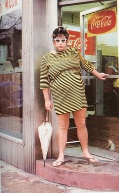 a woman standing in front of a store with her hands on her hips and holding an umbrella