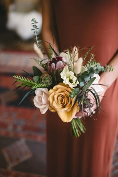 a woman in a red dress holding a bouquet of flowers and greenery on her wedding day