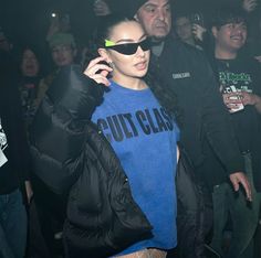 a woman wearing sunglasses and a blue shirt is talking on her cell phone while standing in front of a group of people