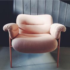 a pink chair sitting on top of a floor next to a wooden paneled wall