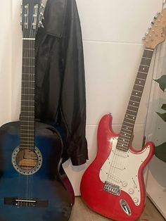 two guitars are sitting next to each other on the floor in front of a coat rack