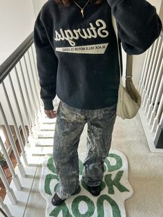 a person standing on a stair case wearing a sweatshirt and jeans with the word stuigus printed on it